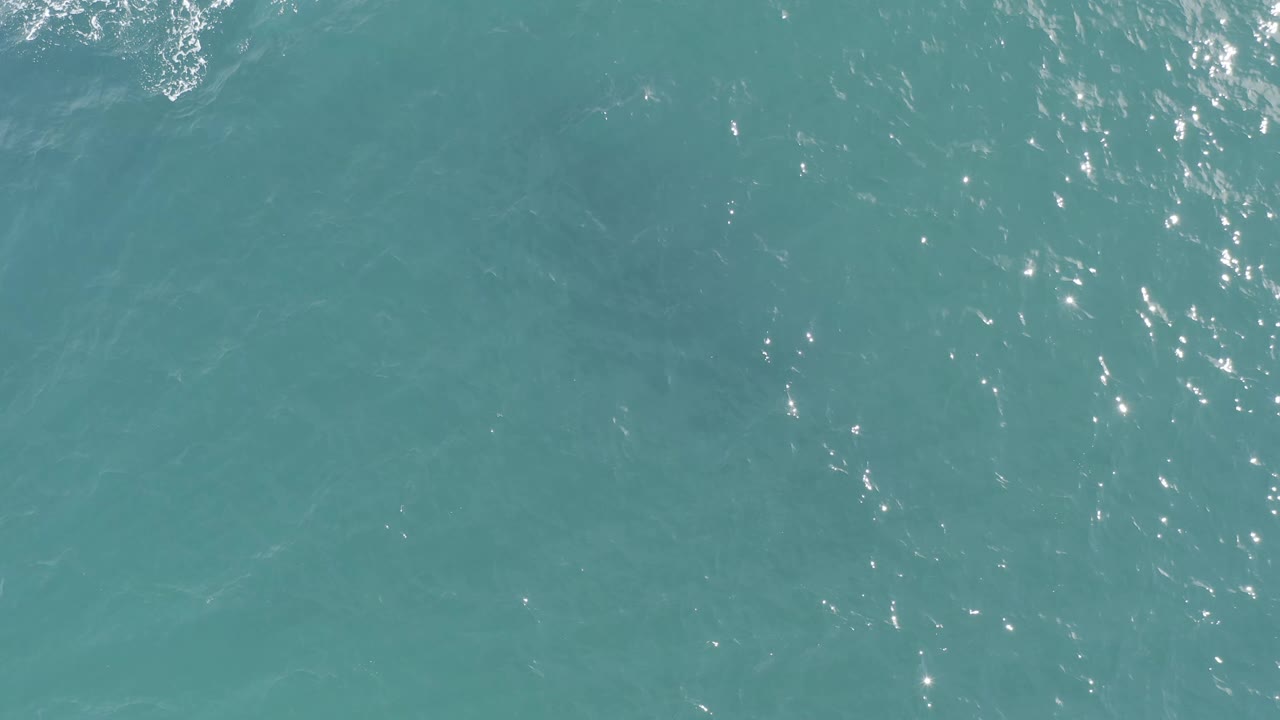 Clear blue-green ocean surface in Baja California Sur, Mexico, with a denser cluster of sun reflections near the lower left and no visible people.