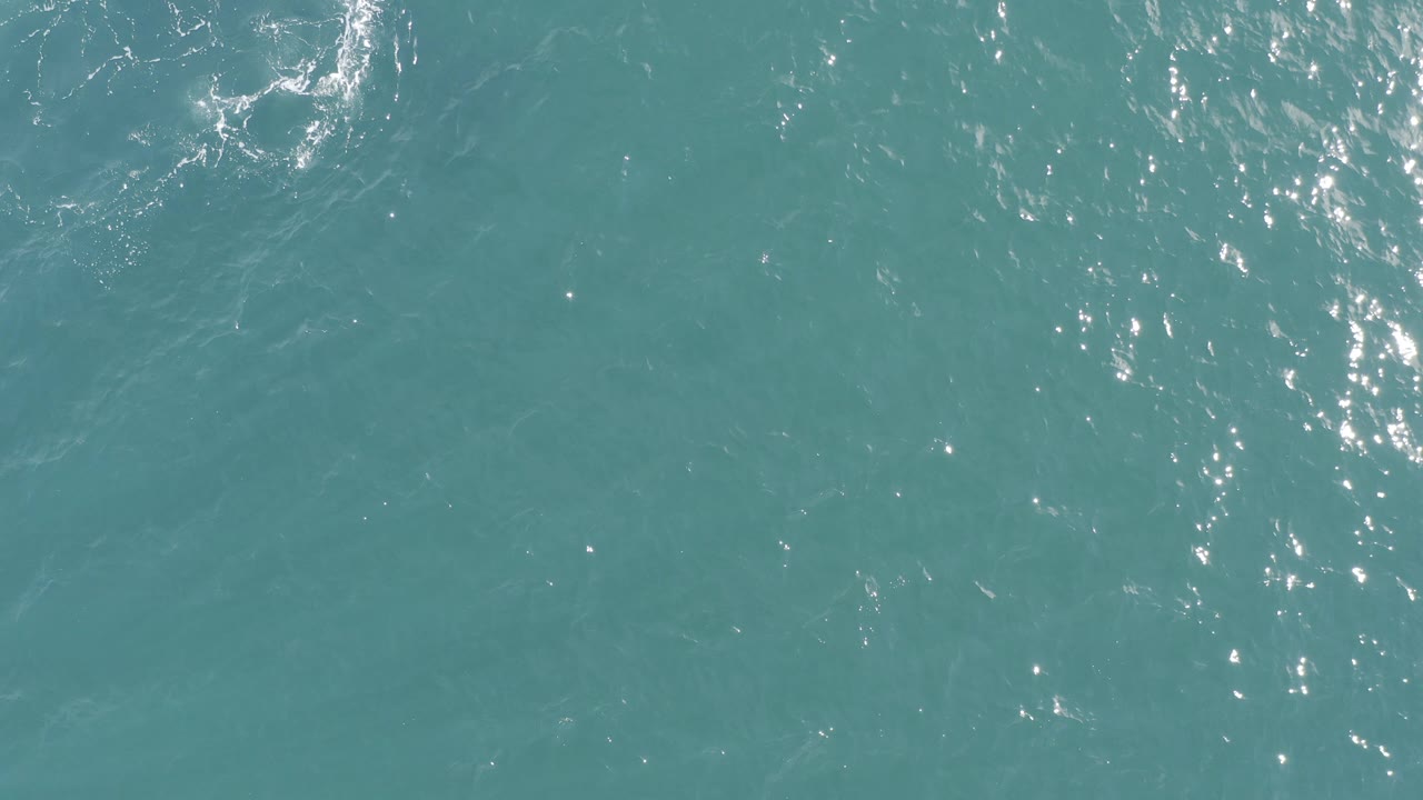 Overhead view of teal ocean water in Baja California Sur, Mexico, with scattered bright glints and faint foam lines, no visible people.