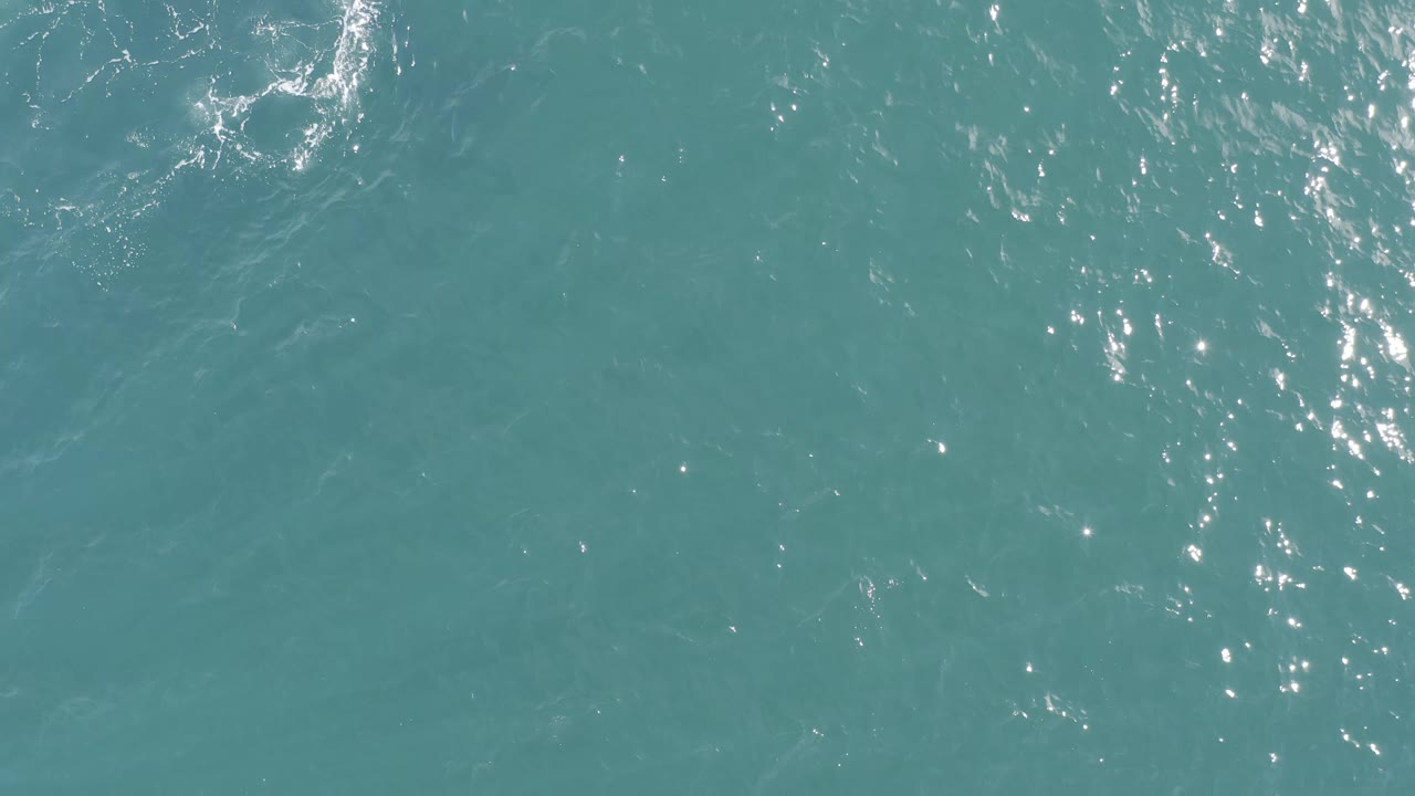 Turquoise ocean surface in Baja California Sur, Mexico, filled with small wavelets and a denser cluster of sunlight reflections near the upper left, no visible people.