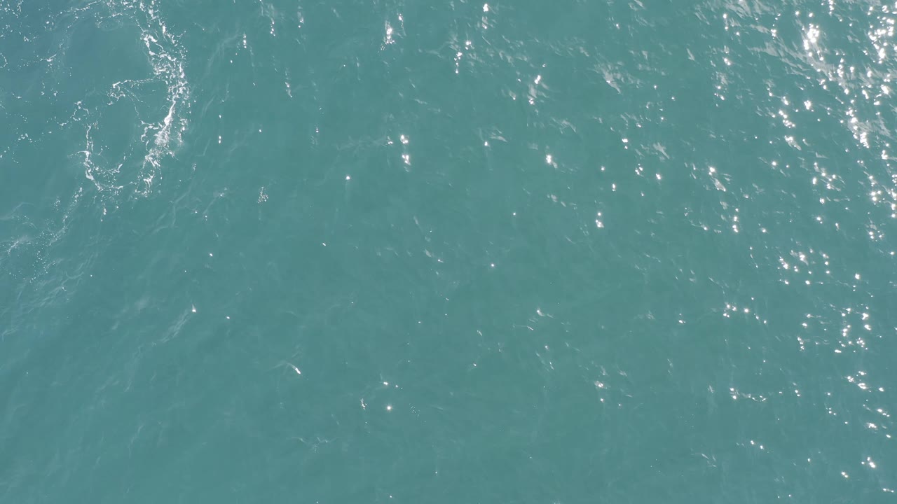 Aerial view of teal water in Baja California Sur, Mexico, with brighter reflection patches along the left side and darker ripple texture across the center, no visible people.