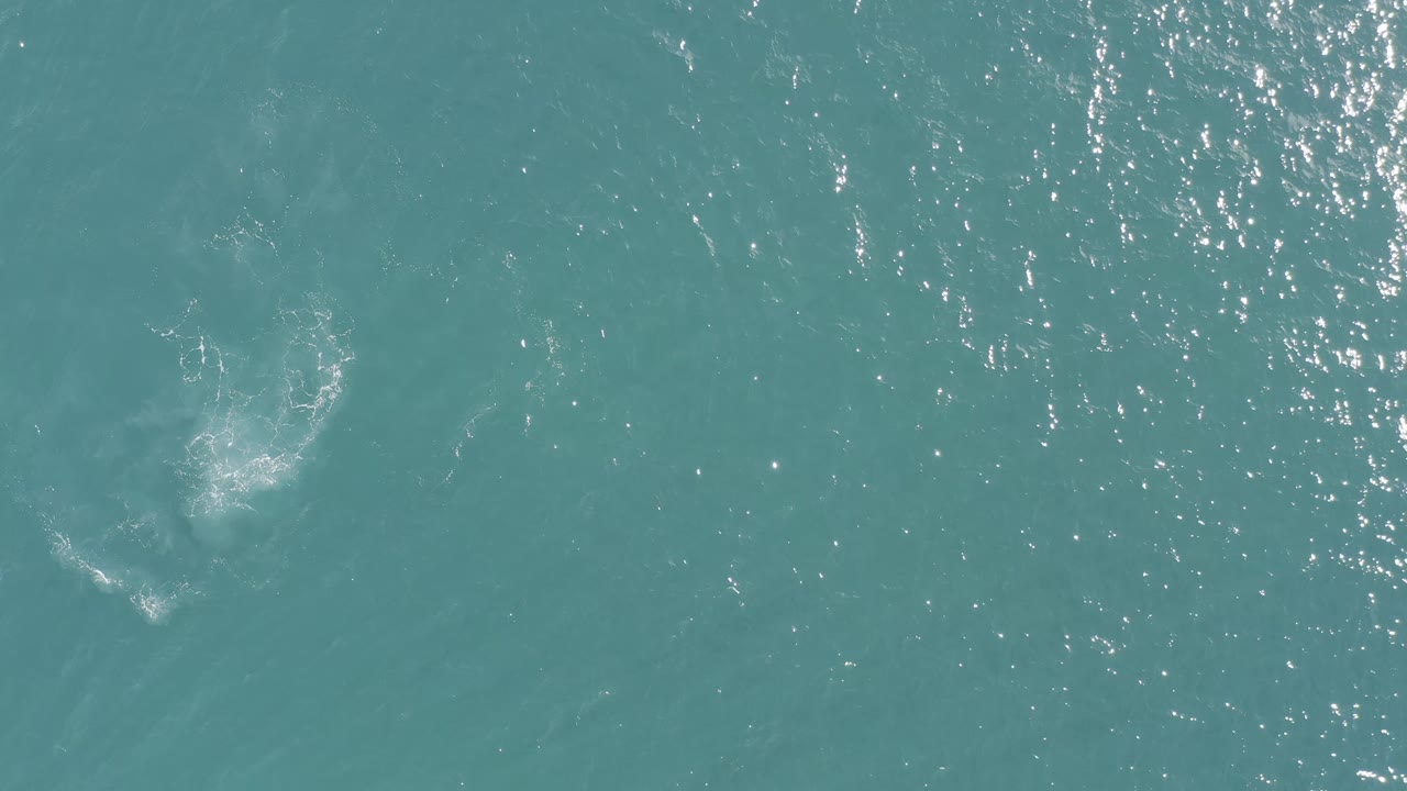 Turquoise ocean surface with white foam and bright sun flecks.
