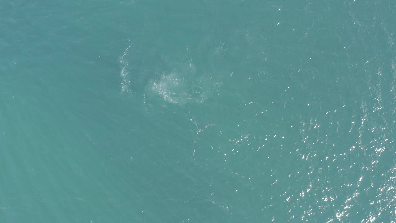 Overhead view of turquoise ocean water in Baja California Sur, Mexico, with a pale cloudy patch near the upper left and no visible people.