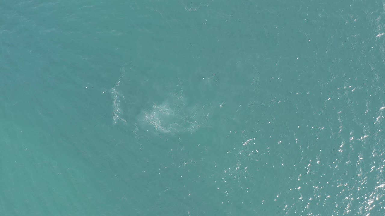 Top-down ocean view in Baja California Sur, Mexico, with scattered bright sparkle and a muted cloudy disturbance in the upper right, with no visible people.
