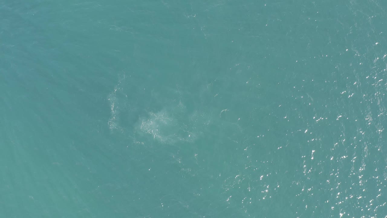Aerial view of turquoise water in Baja California Sur, Mexico, with a soft pale patch lower left and fine surface ripples, with no visible people.