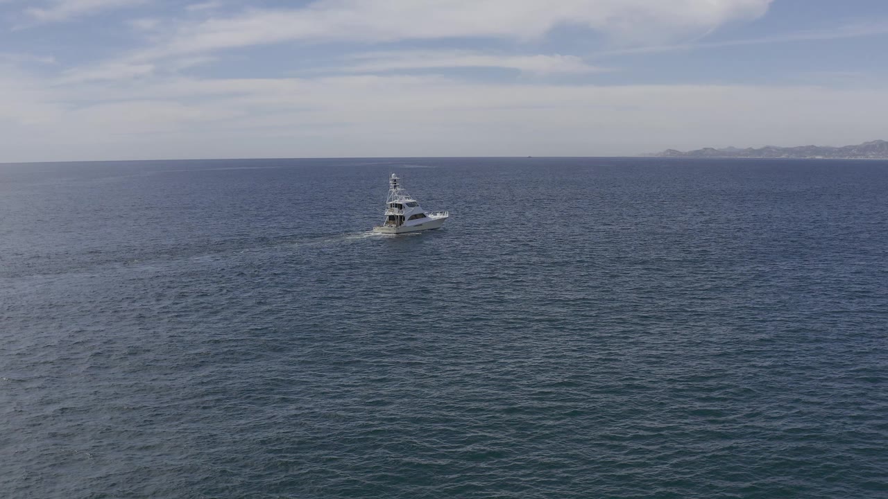 Small white boat on open blue-gray water with distant coast on the horizon.