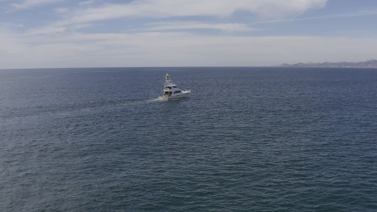The white boat sits near the upper middle of the frame on Baja California Sur water, with its wake stretching left across textured blue sea and no visible people.
