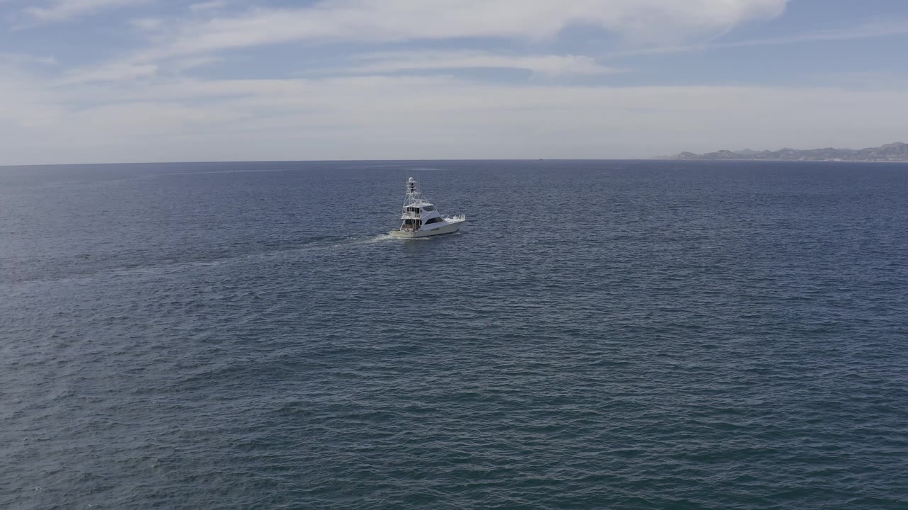 A small white motorboat remains alone on the blue-gray sea in Baja California Sur, Mexico, with the distant coast running along the horizon and no visible people.