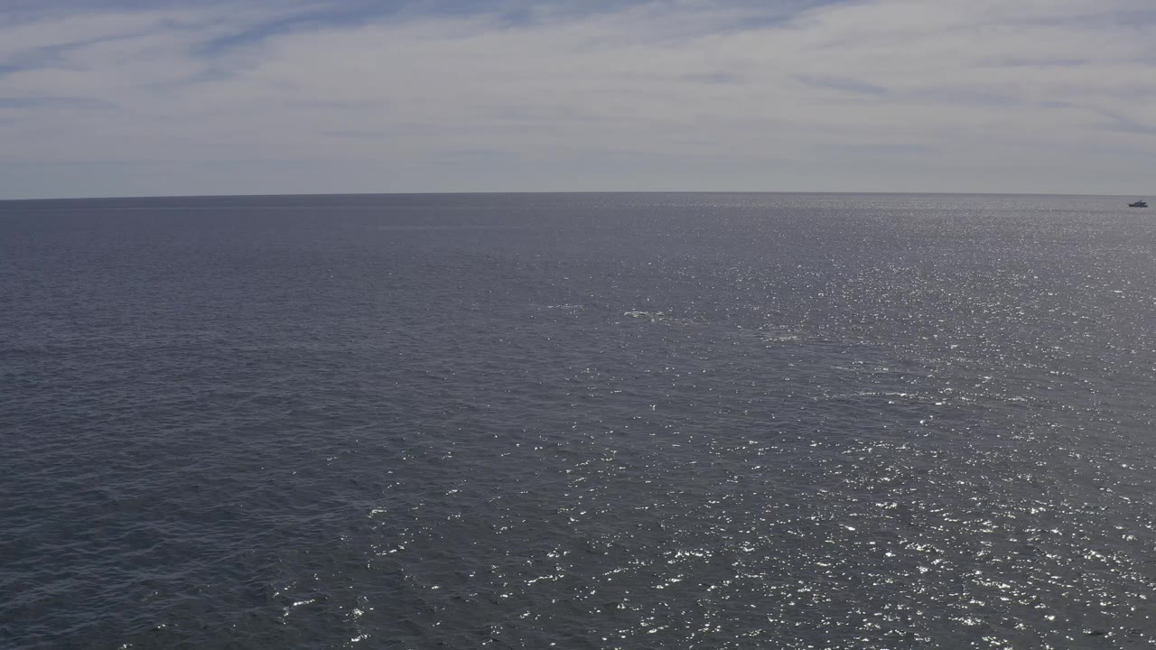 The ocean surface in Baja California Sur, Mexico, fills the frame with a silver glare path, faint surface texture, a tiny distant vessel-like speck near the horizon, and no visible people.