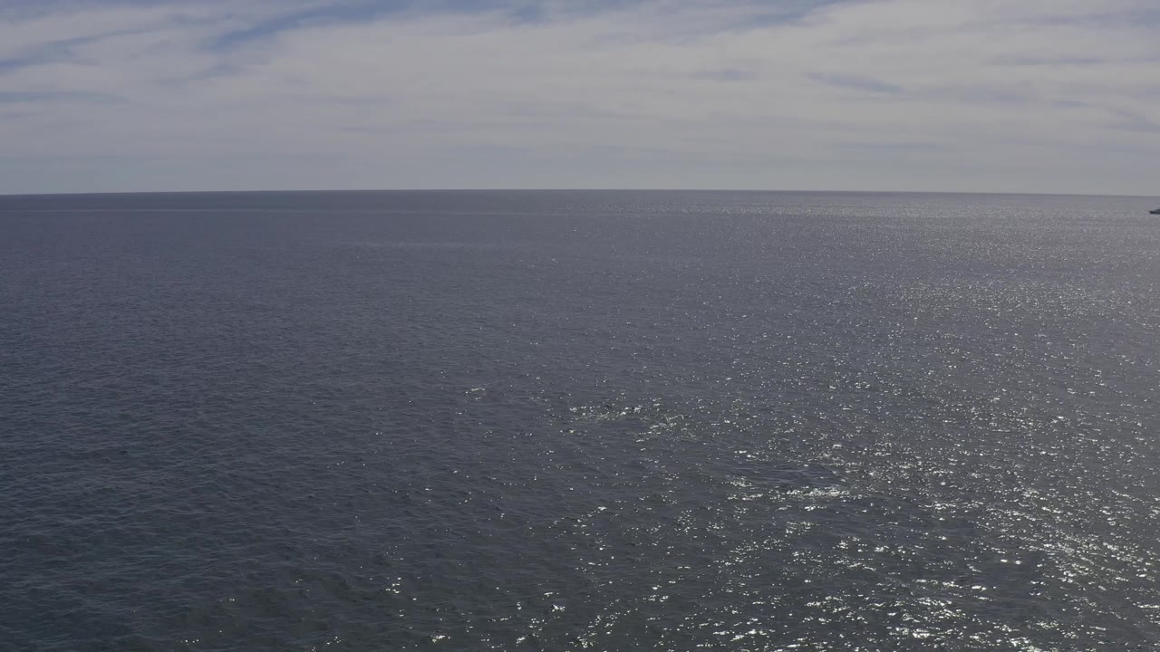 Aerial ocean view in Baja California Sur with textured blue water, a thin horizon line, distant land at the upper edge, and no visible people.
