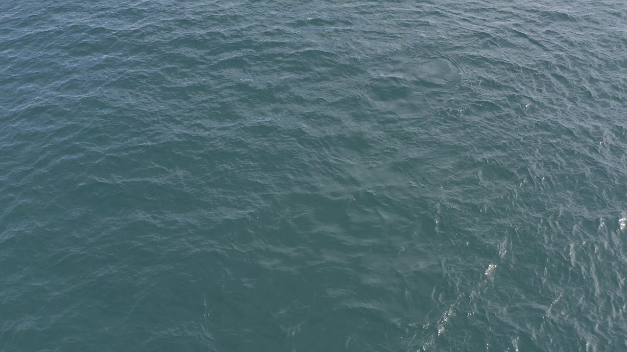 High view over blue-green ocean water in Baja California Sur, Mexico, with fine ripples, faint foam lines, and no visible people.
