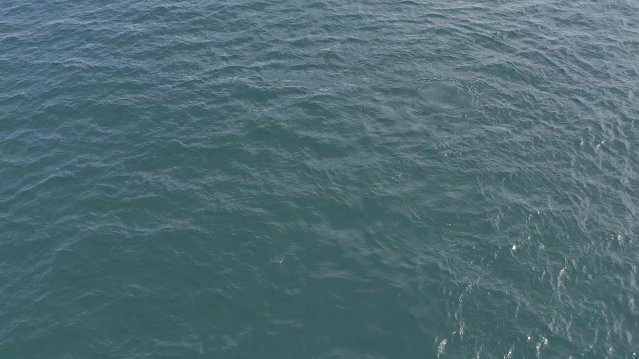 Frame-filling Baja California Sur ocean water with soft wave lines, muted teal color, and small bright reflections, with no visible people.