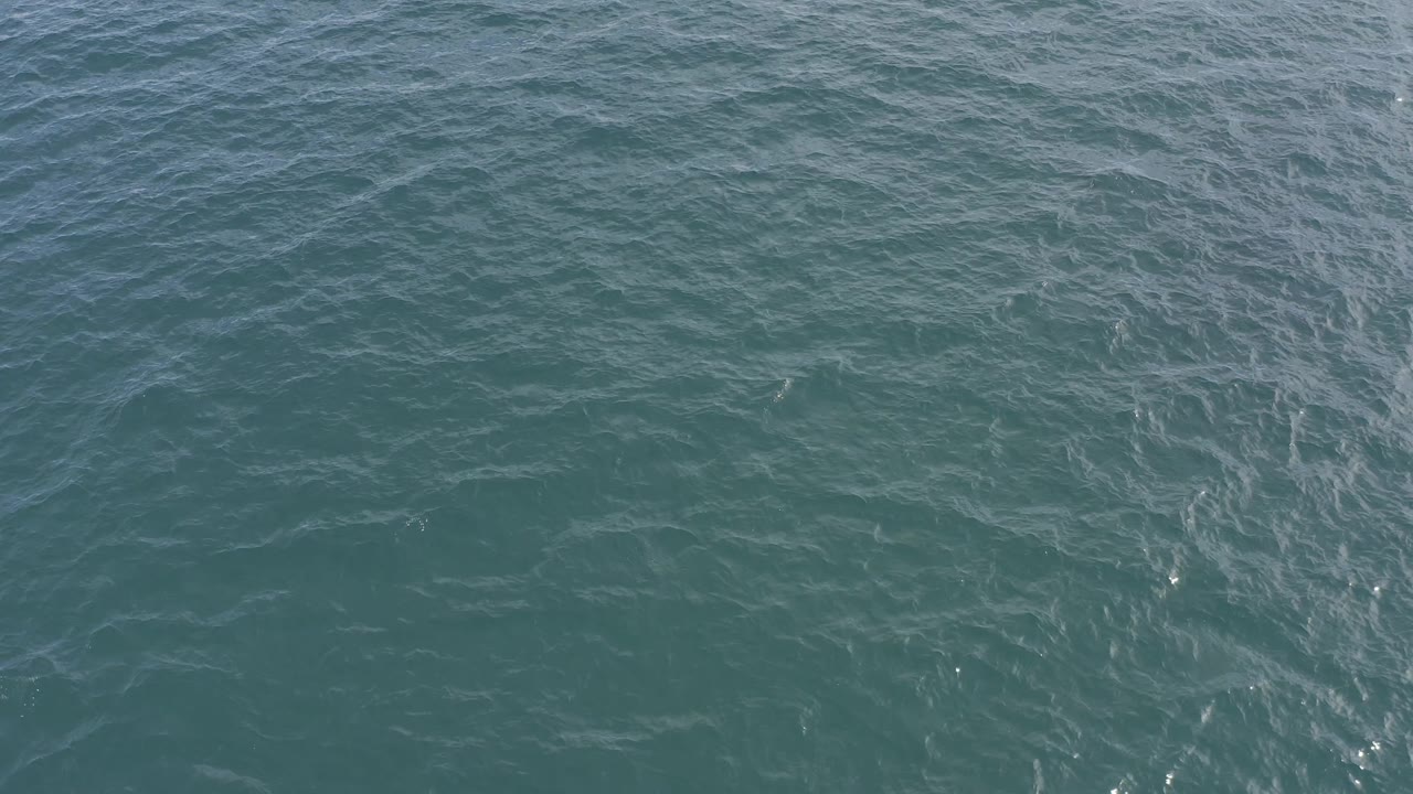 Green-blue ocean water in Baja California Sur, Mexico, shows fine wave lines and subtle white streaks across the surface, with no visible people.