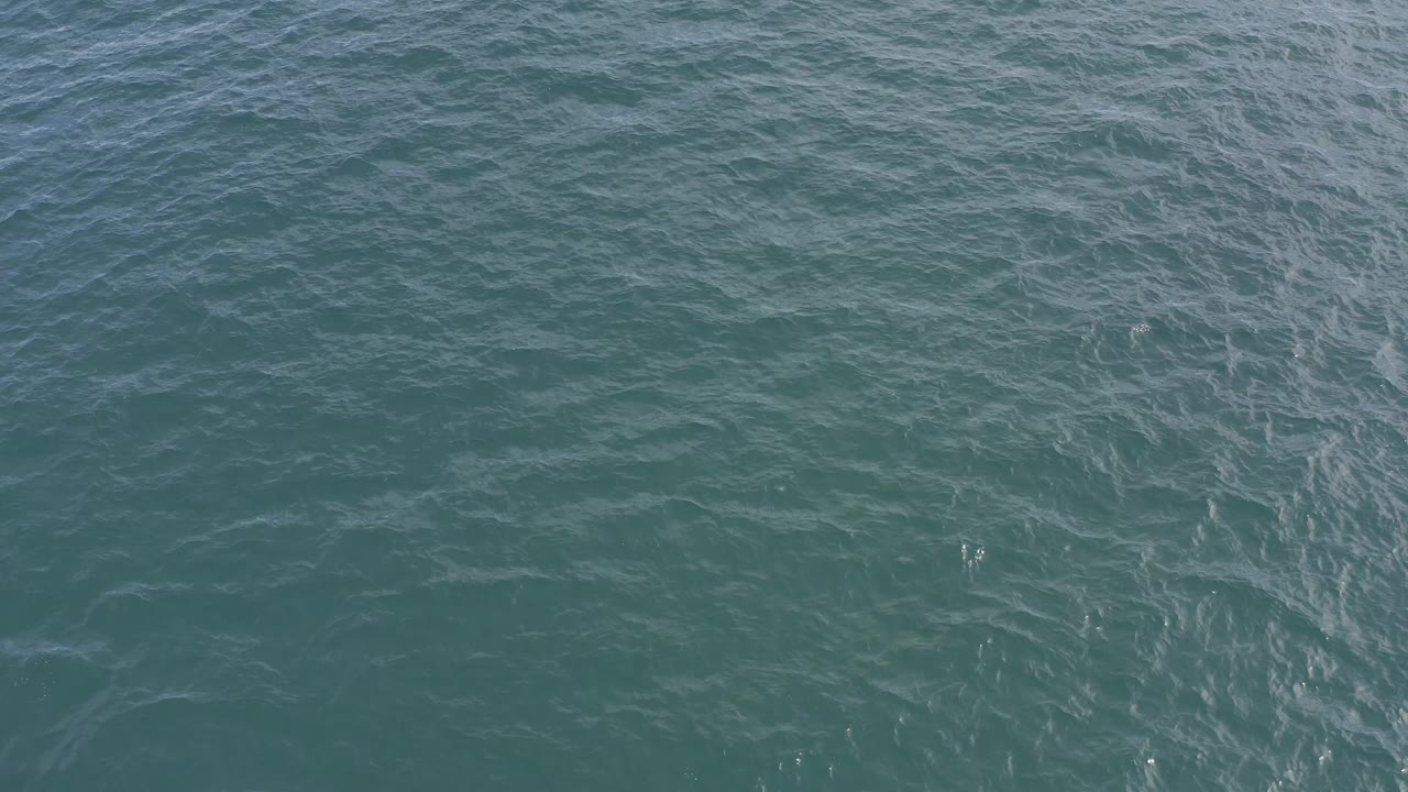 Mid-clip frame of teal sea surface in Baja California Sur, Mexico, with wider ripple bands and scattered pale streaks, with no visible people.