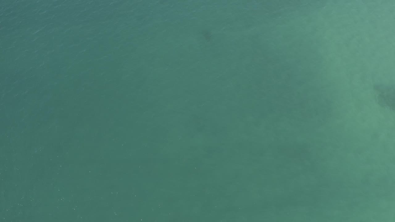 Turquoise water with muted underwater patches and small surface flecks.