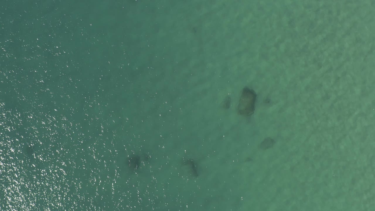 Overhead turquoise water with dark submerged patches and sun glints