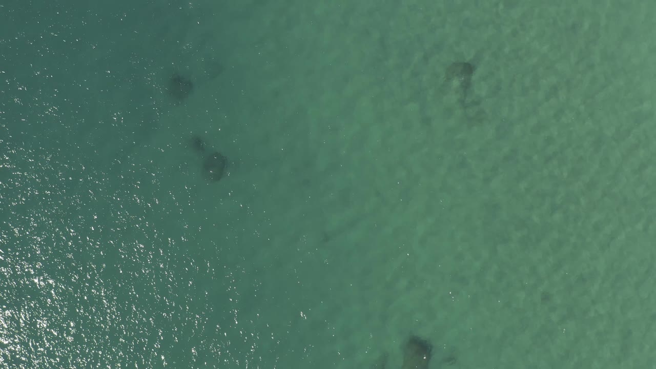 Overhead Baja California Sur sea surface with blue-green water, small ripples, dark reef-like marks under the surface, and no visible people.
