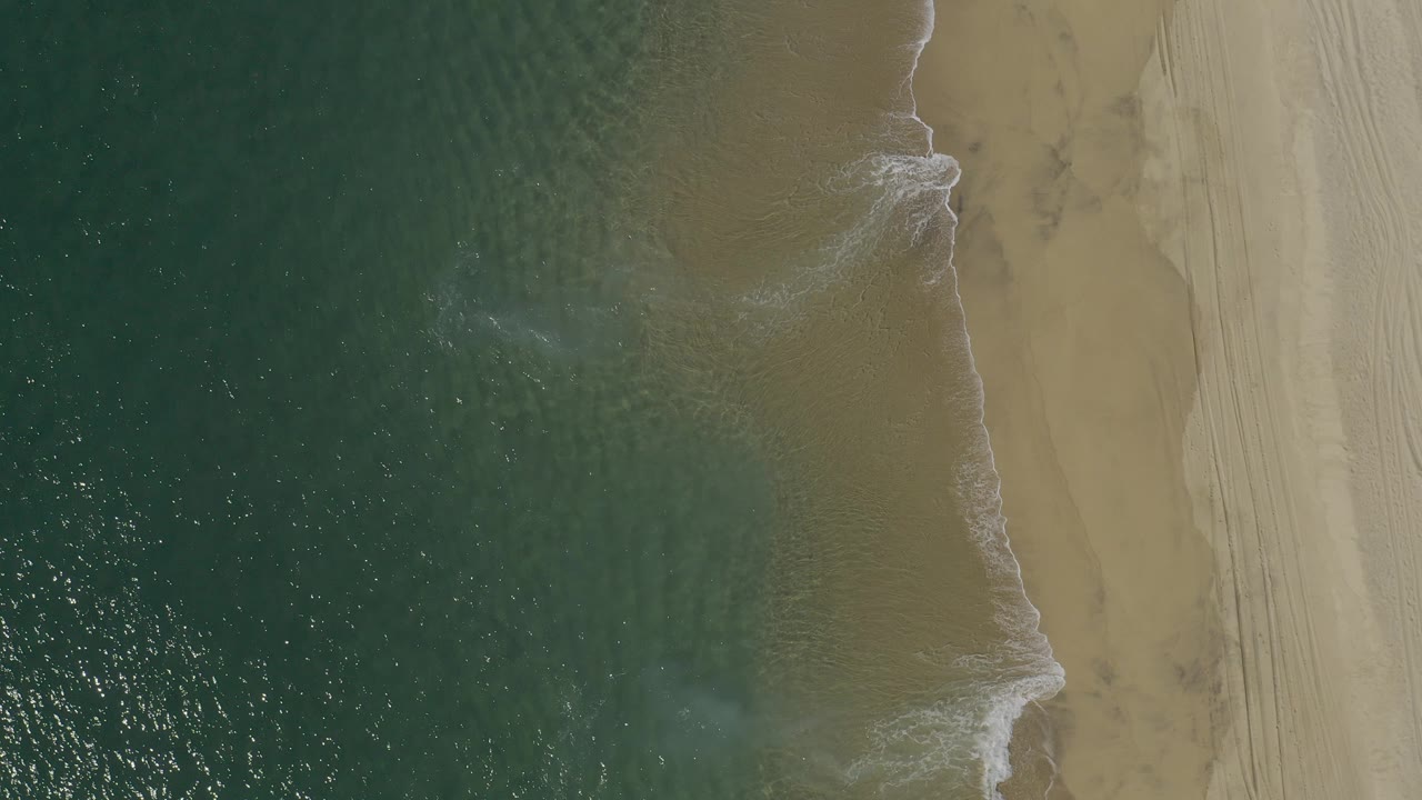 Overhead view of waves meeting a sandy beach.