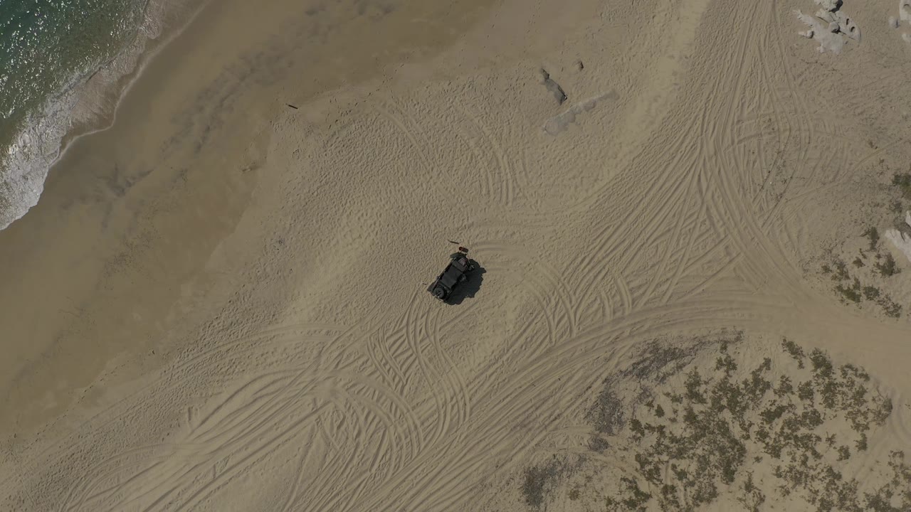 Drone view of tracked sand with a dark object and water along the upper left edge.