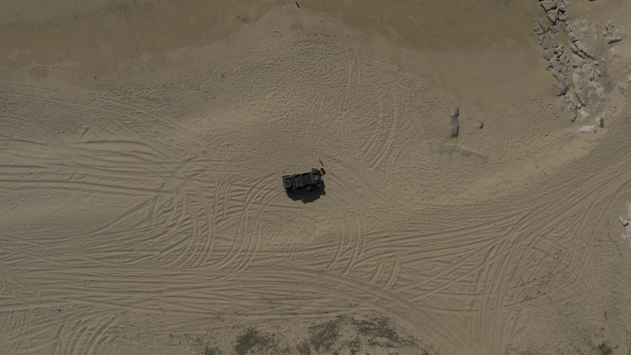 Overhead sandy terrain with tire tracks and a dark off-road vehicle.