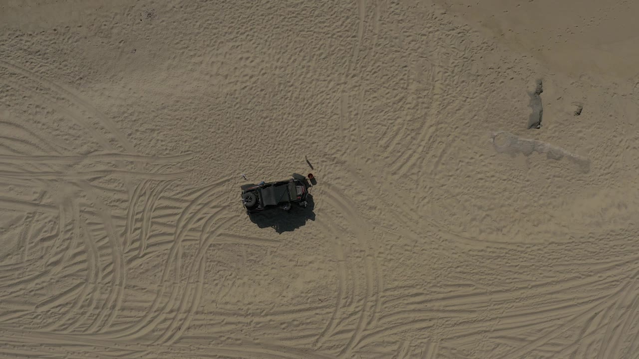 Overhead view of a dark object on tracked sand.