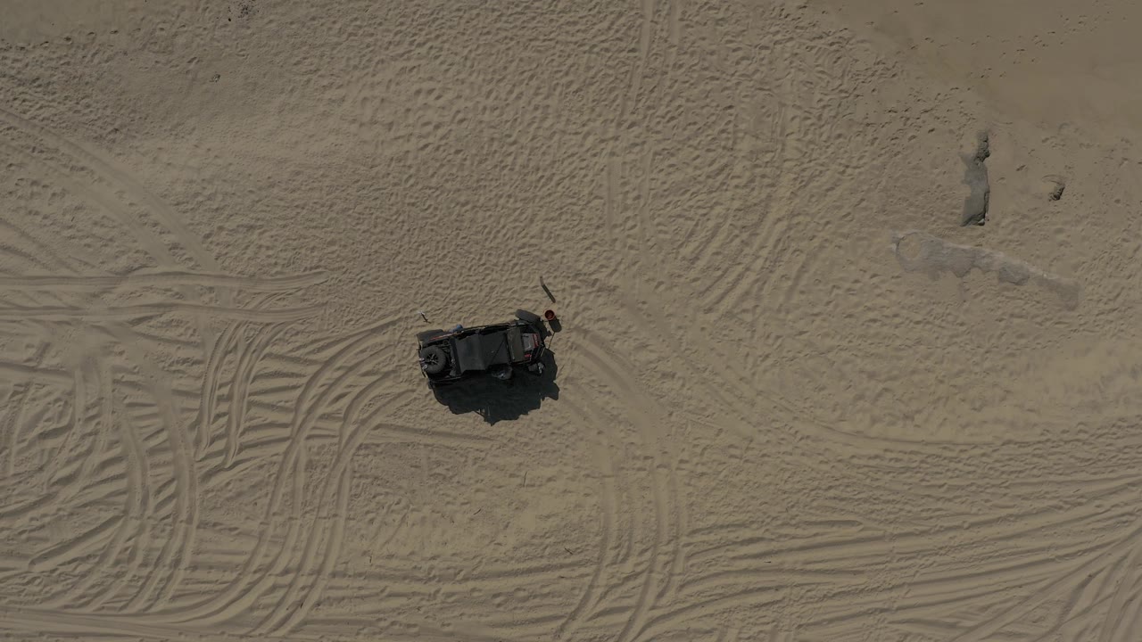 Overhead desert frame in Baja California Sur Mexico showing a small dark object below patterned tire marks and a pale patch of sand, with no visible people.