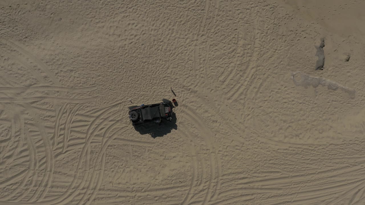 Baja California Sur Mexico aerial frame with the dark object near the lower left of a broad sand area crossed by tire tracks, with no visible people.