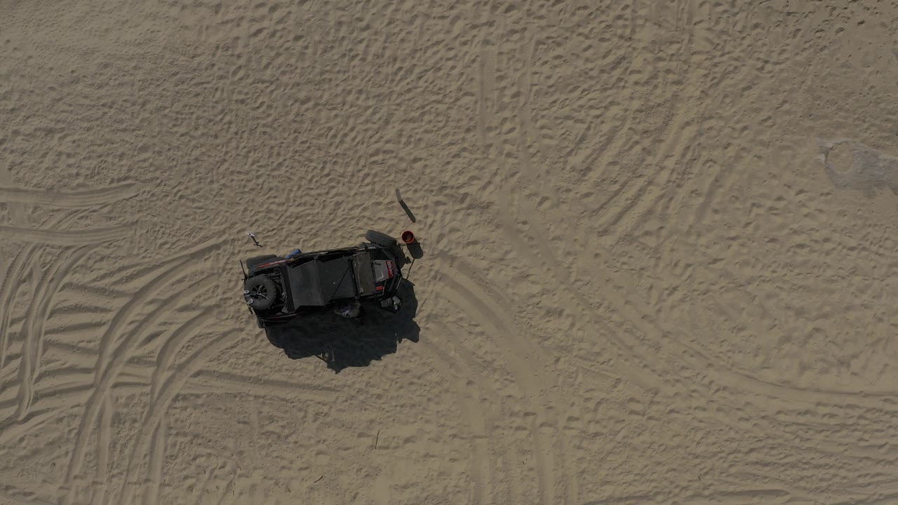 A black off-road vehicle sits near sweeping tire marks on open sand in Baja California Sur, with no visible people and no horizon in frame.