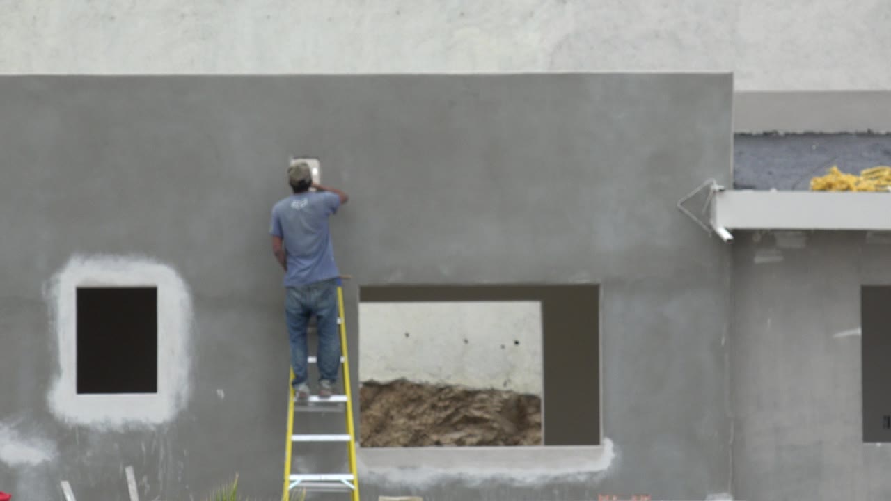 Man on yellow ladder working on a gray wall.