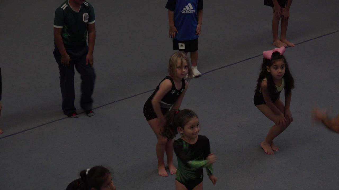 Several children remain grouped on the gray mat in Cabo San Lucas, Mexico, while a child in a green and black outfit moves through the foreground.