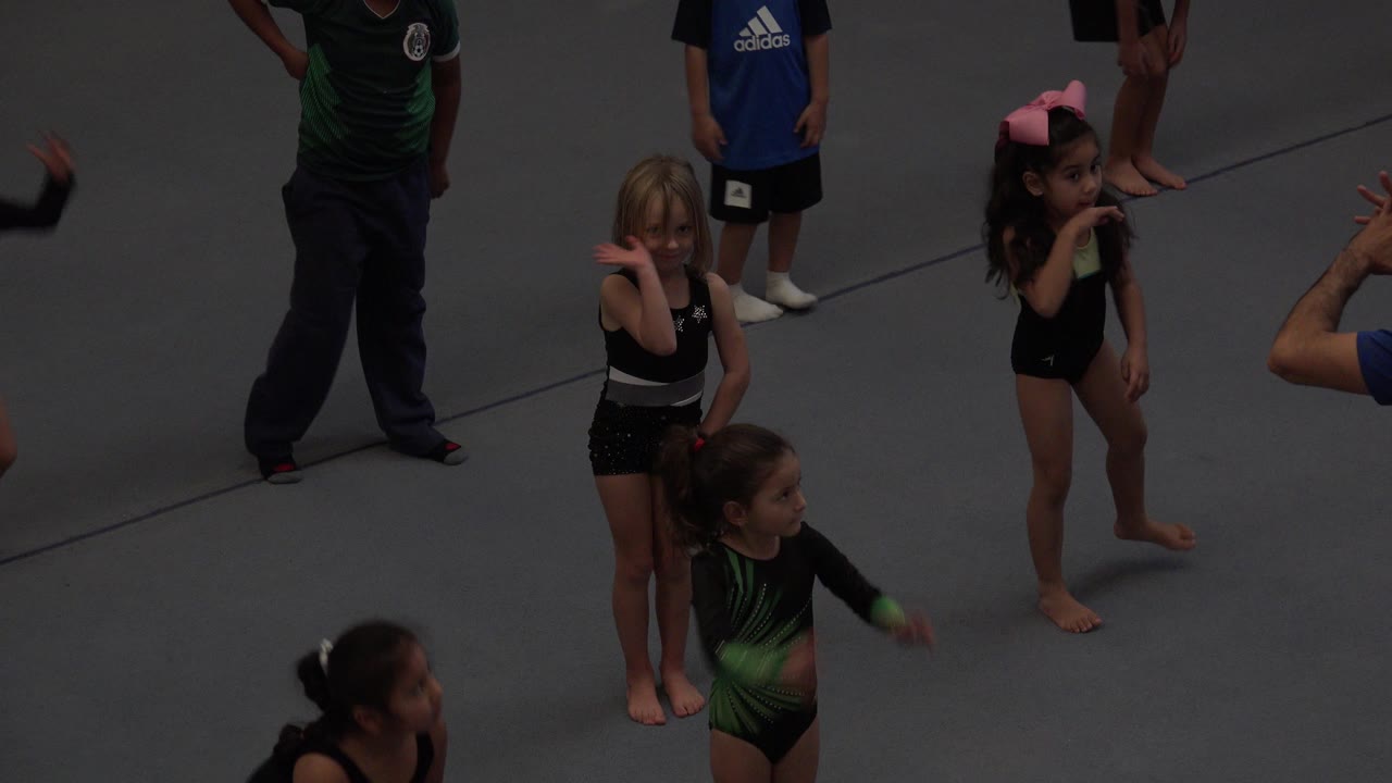 Children and an adult on a gymnastics mat with raised hands visible.