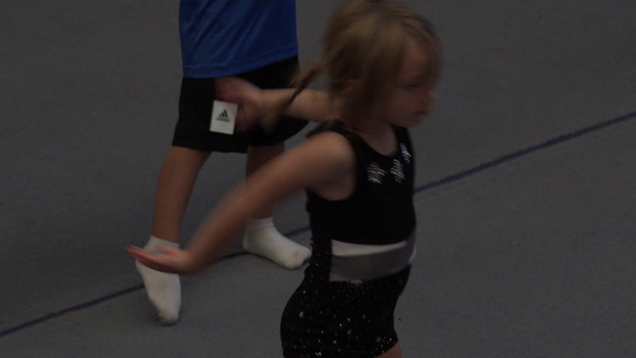 Young girl in a black outfit moving on a grey mat beside socked legs.