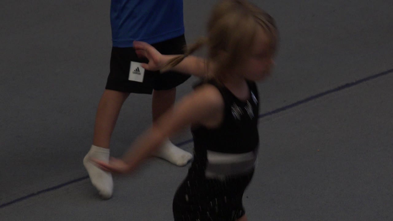 A blurred young girl in black moves across the grey mat in Cabo San Lucas, Mexico, while partial legs and white socks remain visible behind her.