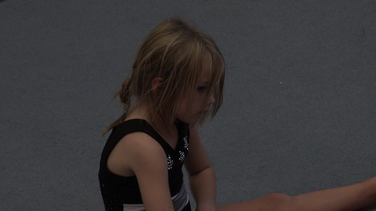 Young girl in a black leotard seated on a gray floor.