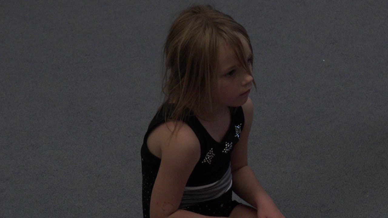 Young girl seated on gray sand in a black bathing suit.