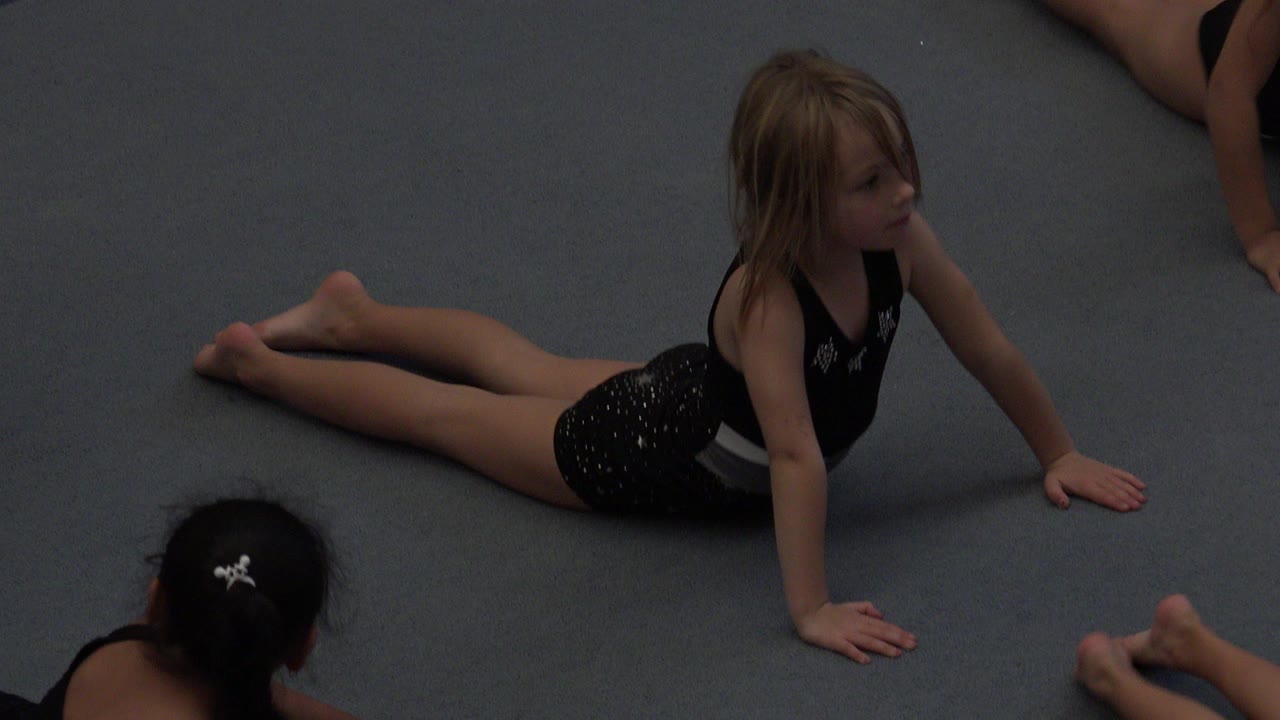 Young girl lying on a blue padded floor during a class activity.