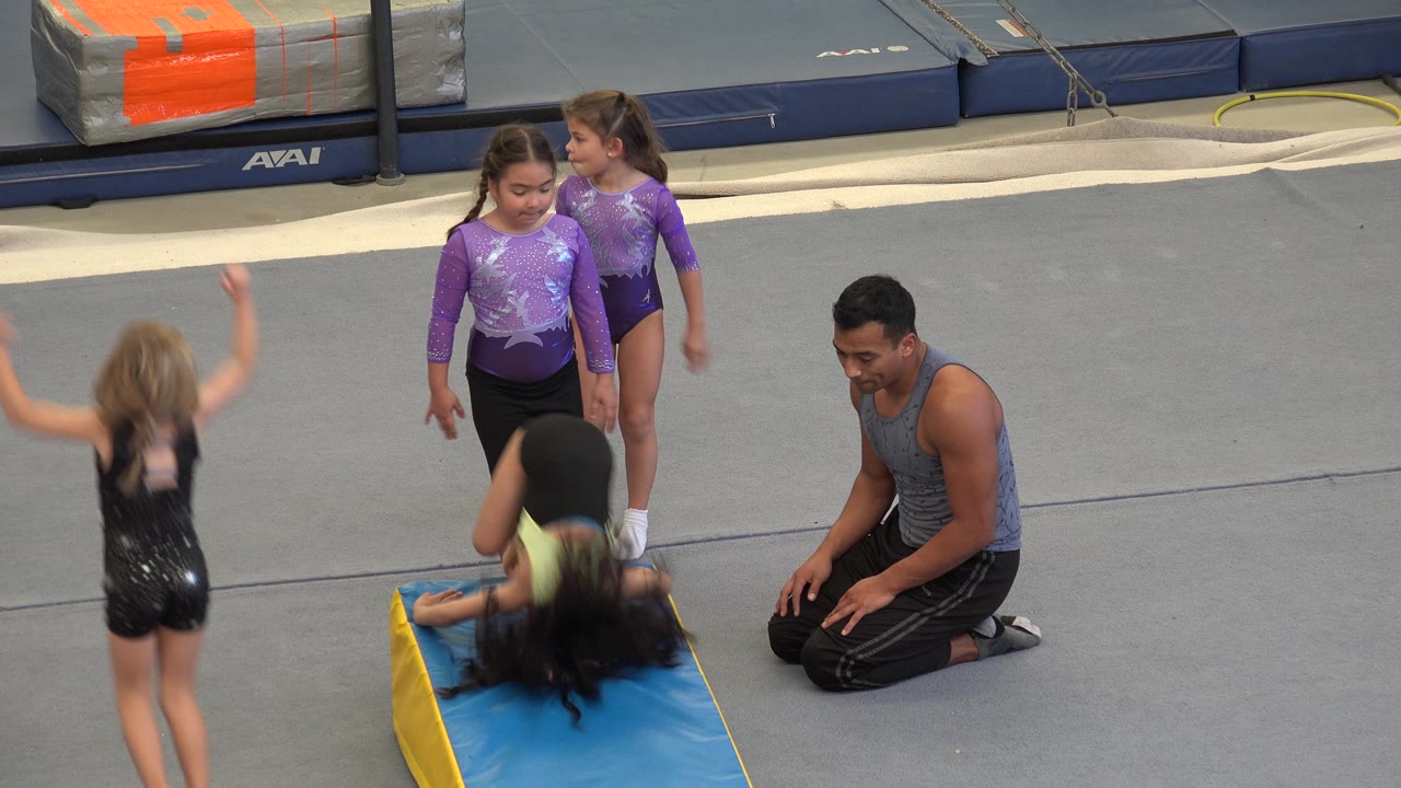 A child flips onto the blue wedge mat while others watch.