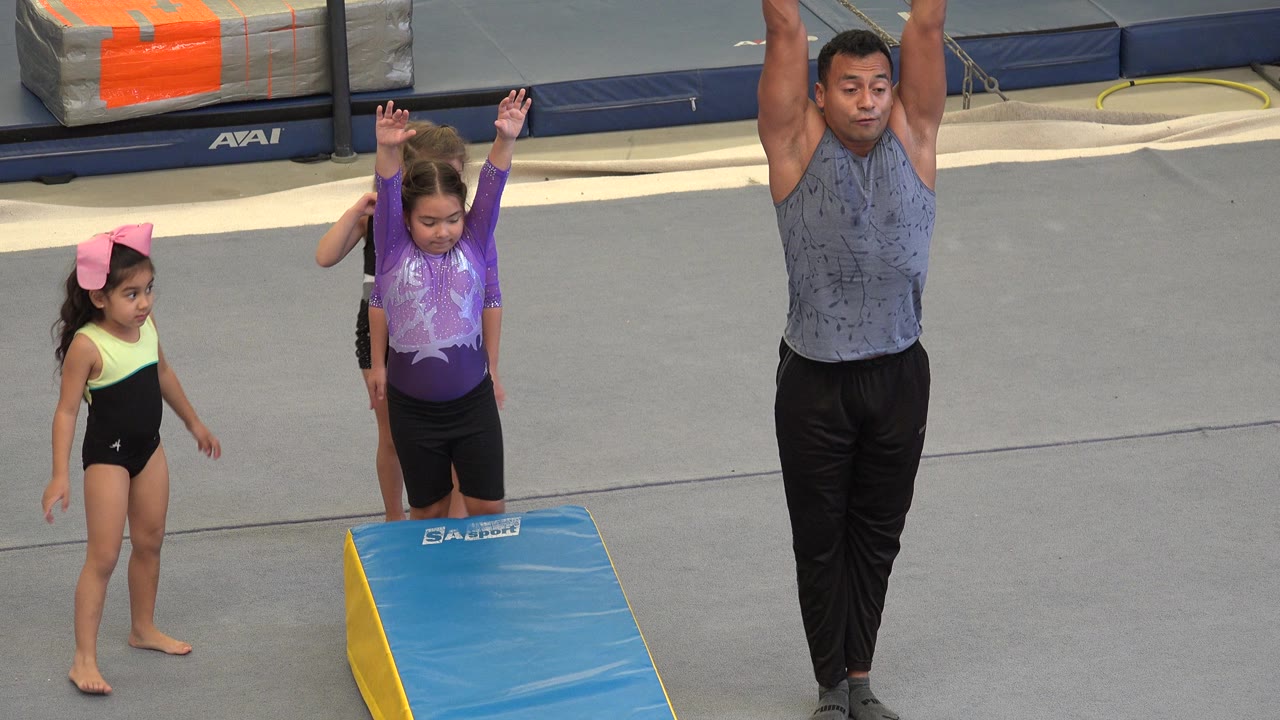 Coach and young gymnasts standing beside a blue wedge mat.