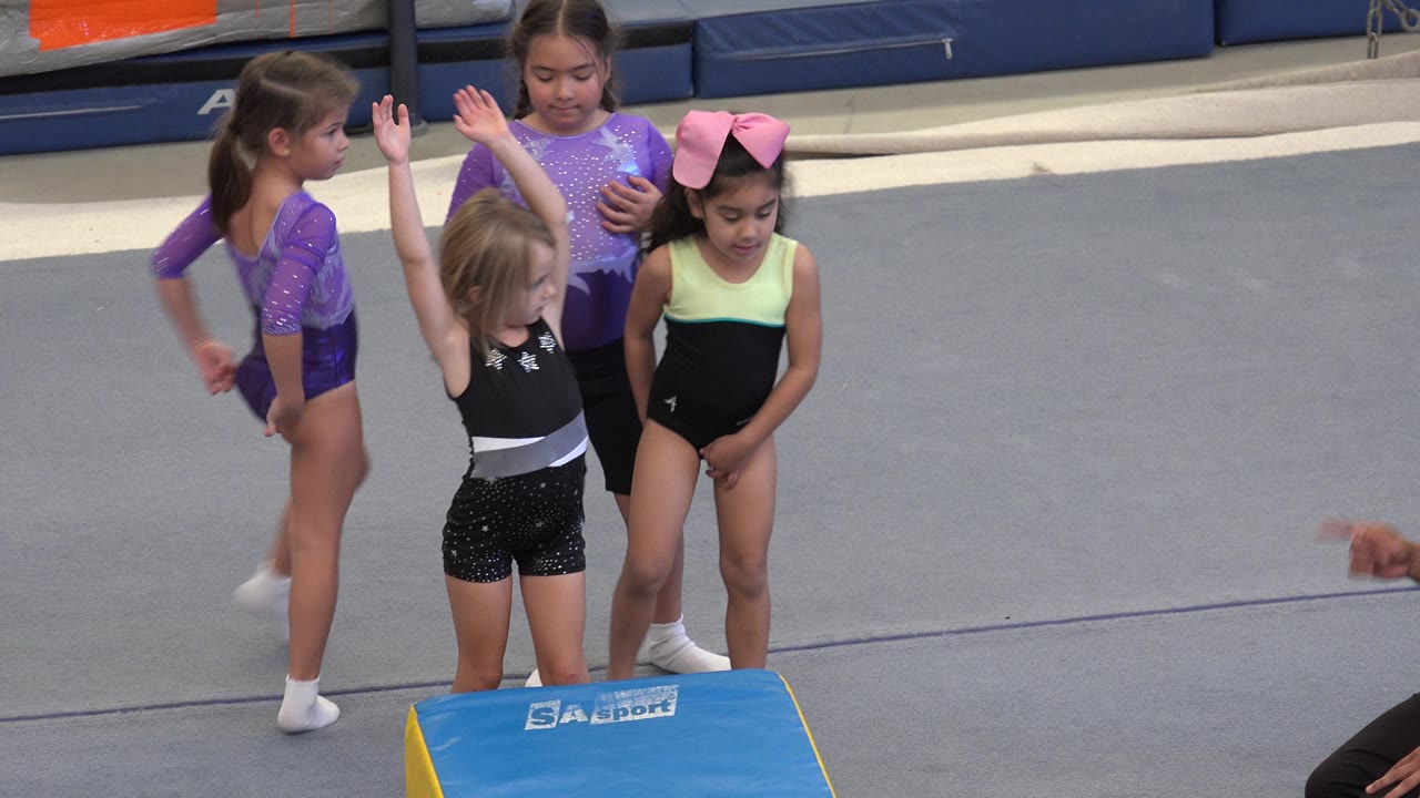Three girls stand by the mat, one with both hands raised.