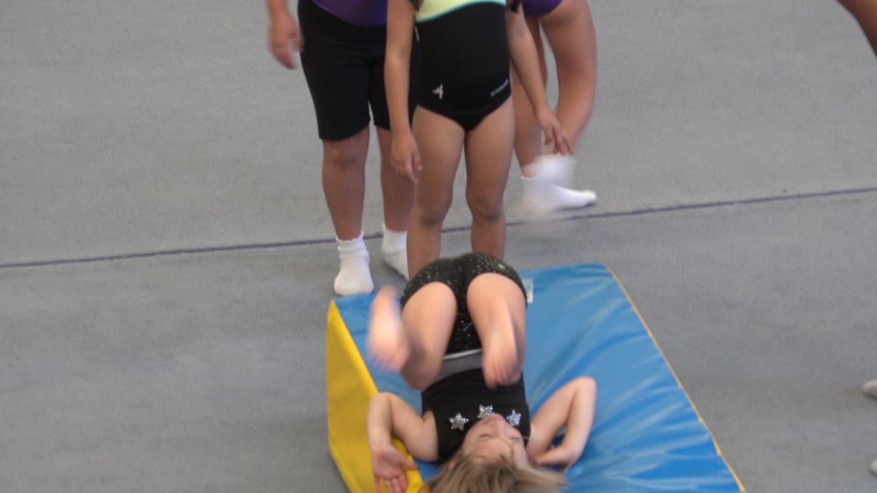 In Cabo San Lucas, Mexico, the girl is curled backward on the blue mat while nearby helpers and children stand close to the exercise area.