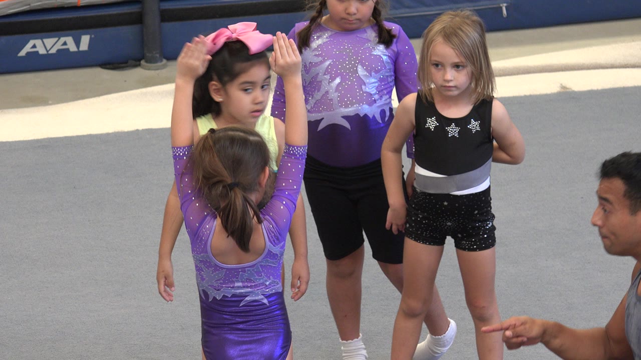 Trainer and children around a young gymnast preparing to somersault.