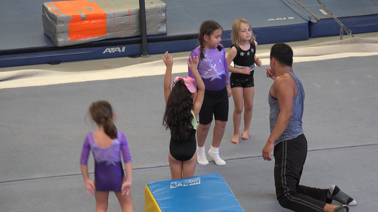 Children and a kneeling coach gather near a gymnastics wedge mat.