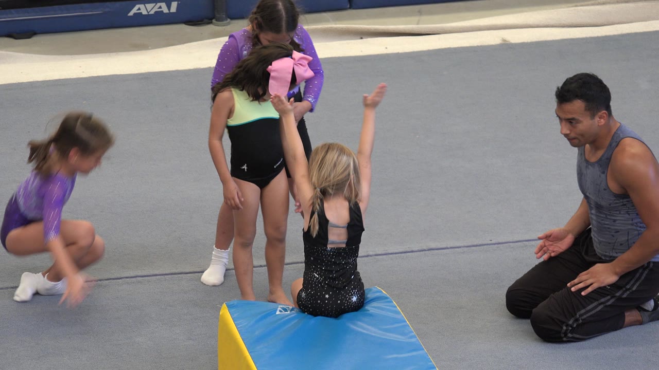 One girl crouches low beside two teammates at the wedge mat as the kneeling coach watches from the right in Cabo San Lucas, Mexico.