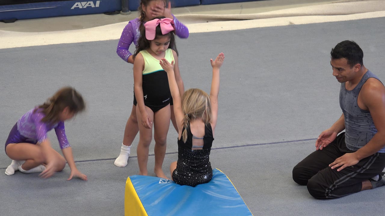 Children wait around a wedge mat while a coach kneels nearby.