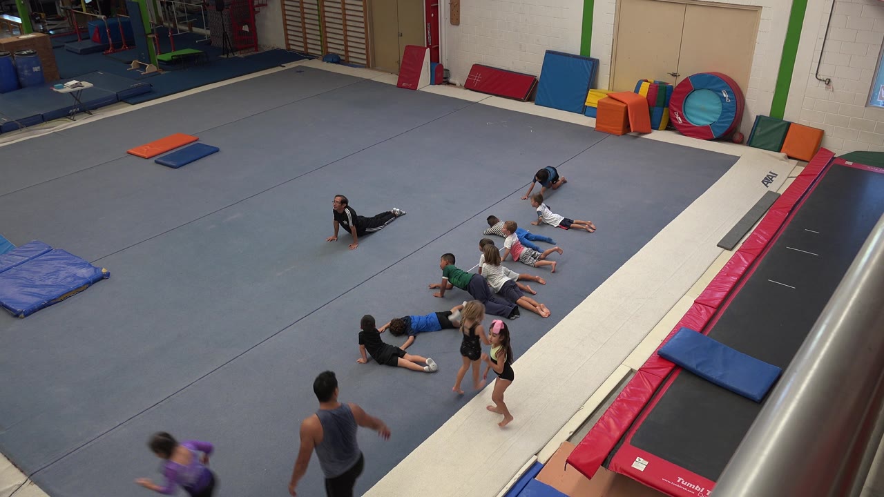 Children lie and kneel near the tumbling lane with gym equipment behind them.