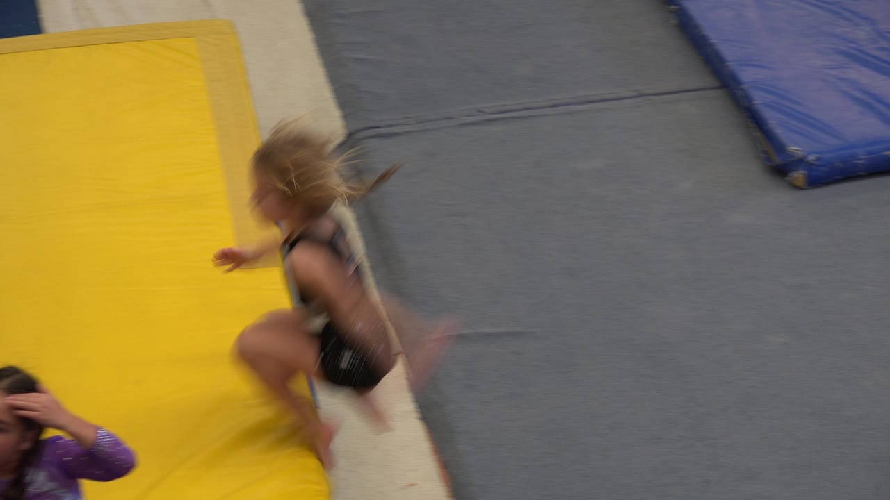Child landing on a yellow gym mat beside other children