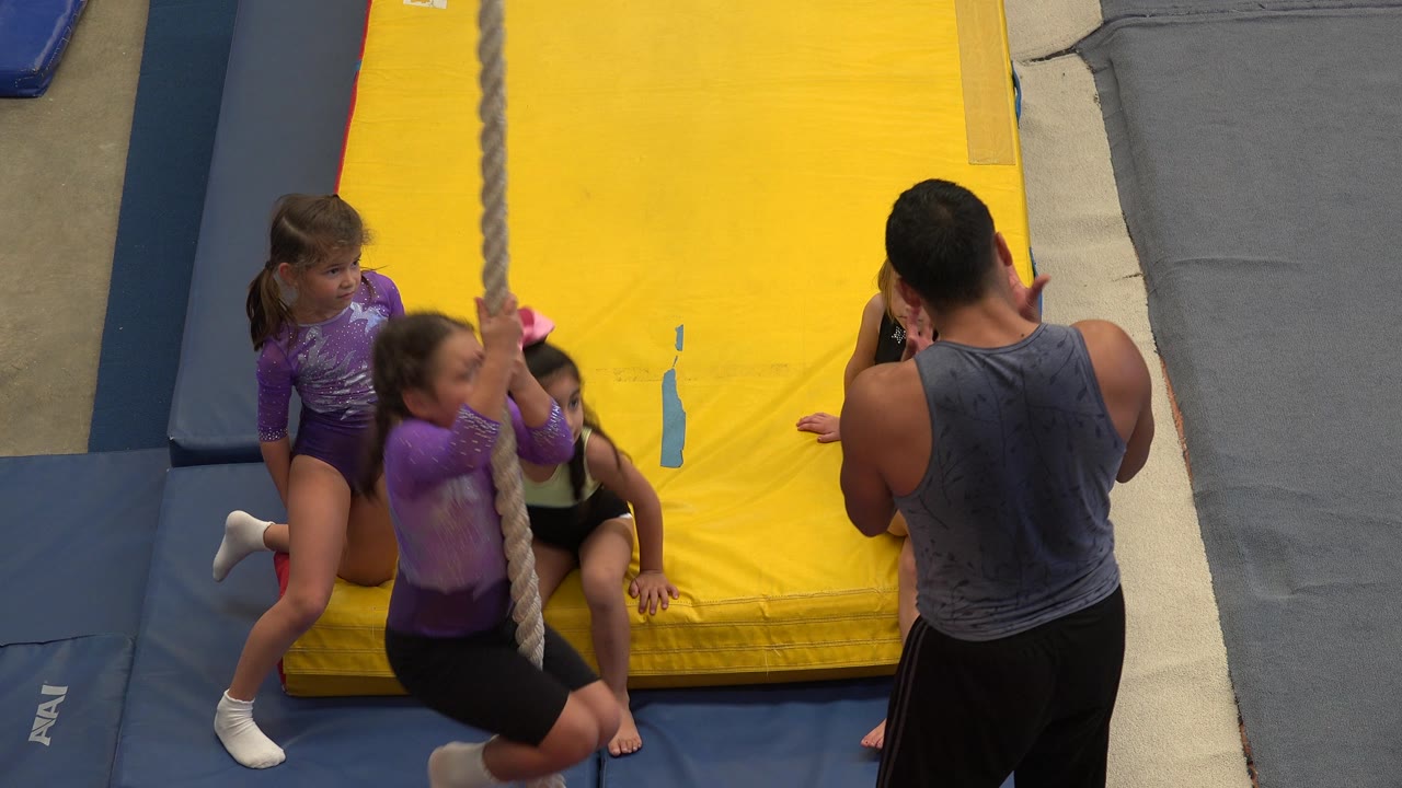 Children sit and kneel around the rope while the instructor observes.