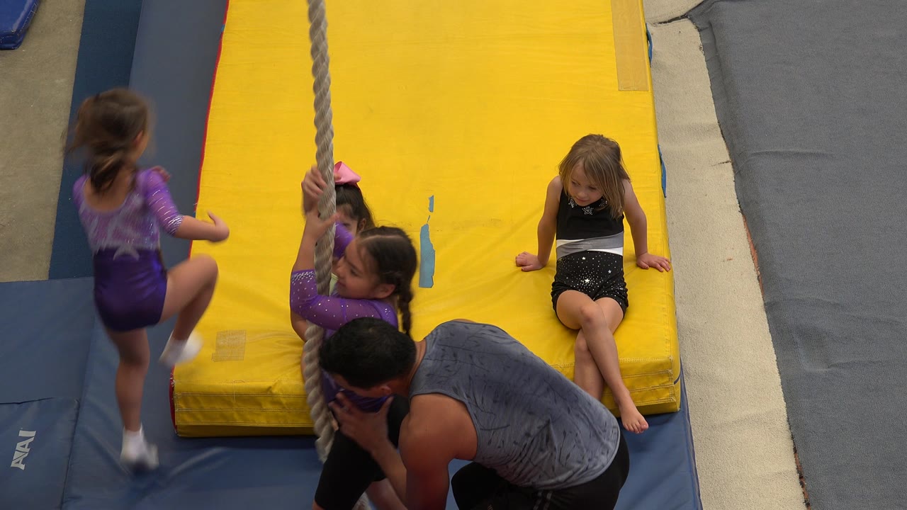 A girl in a purple leotard steps beside the rope while the crouching instructor watches and other children wait on the yellow mat in Cabo San Lucas.