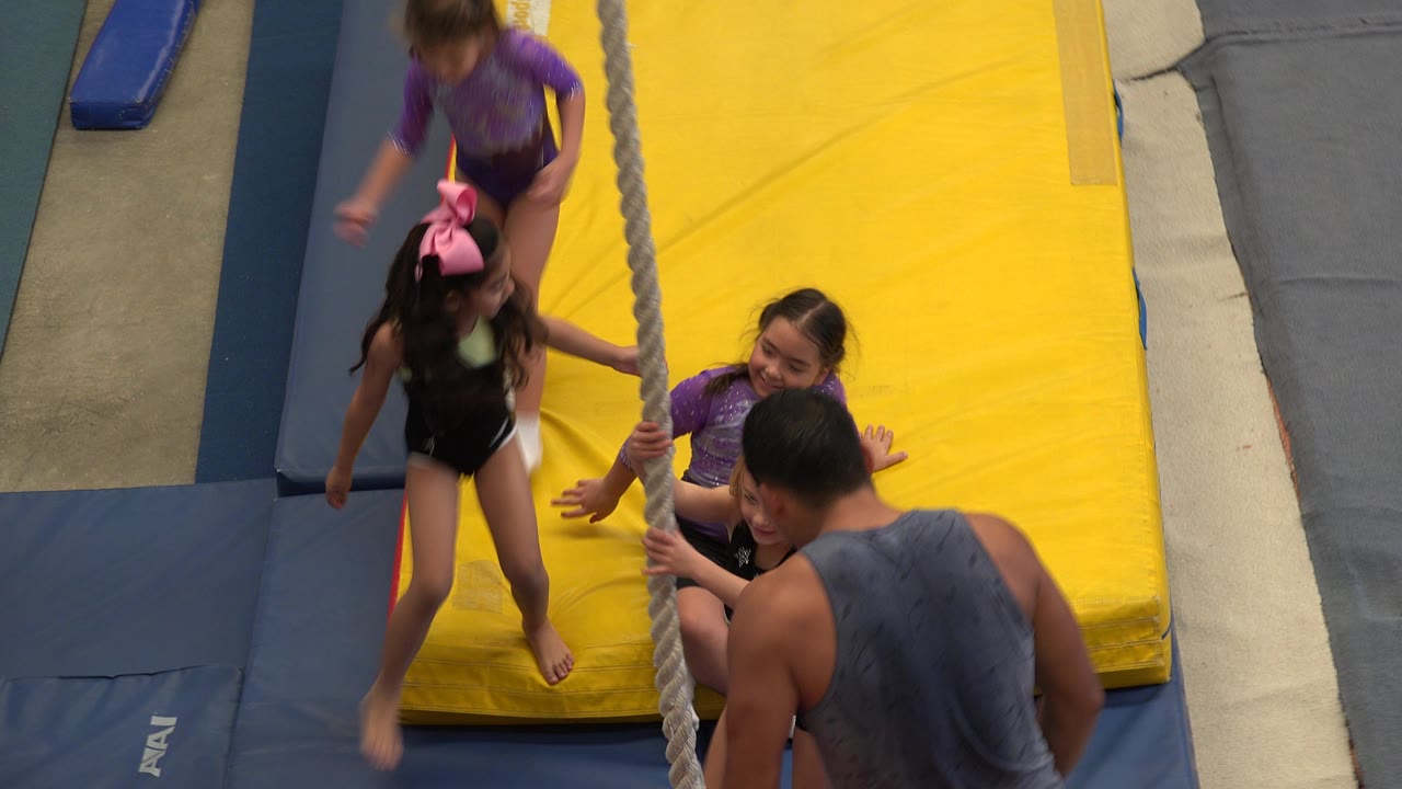 Young girls gather near a hanging rope on gym mats.