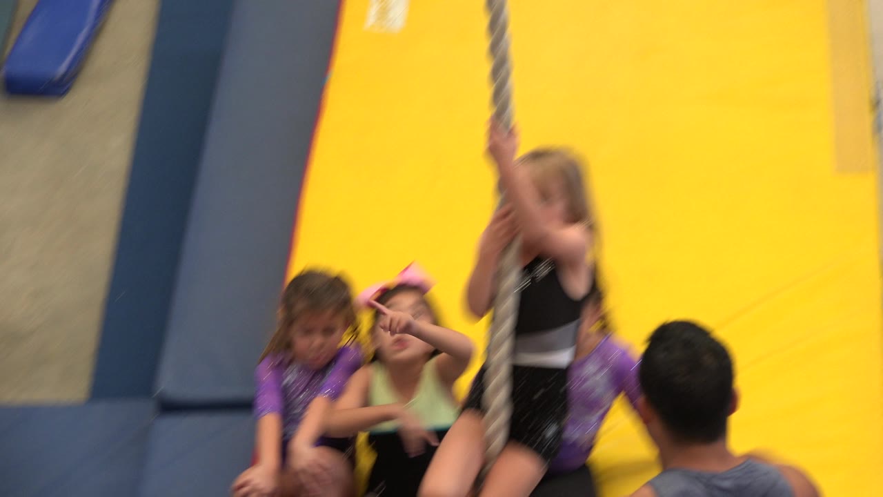 A girl stands holding the rope while other children sit on the mat.