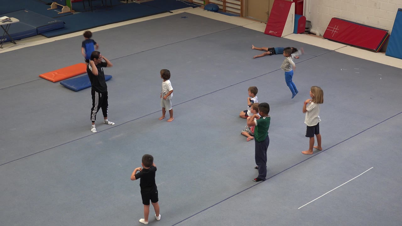 Children and an instructor on a padded gymnastics floor.